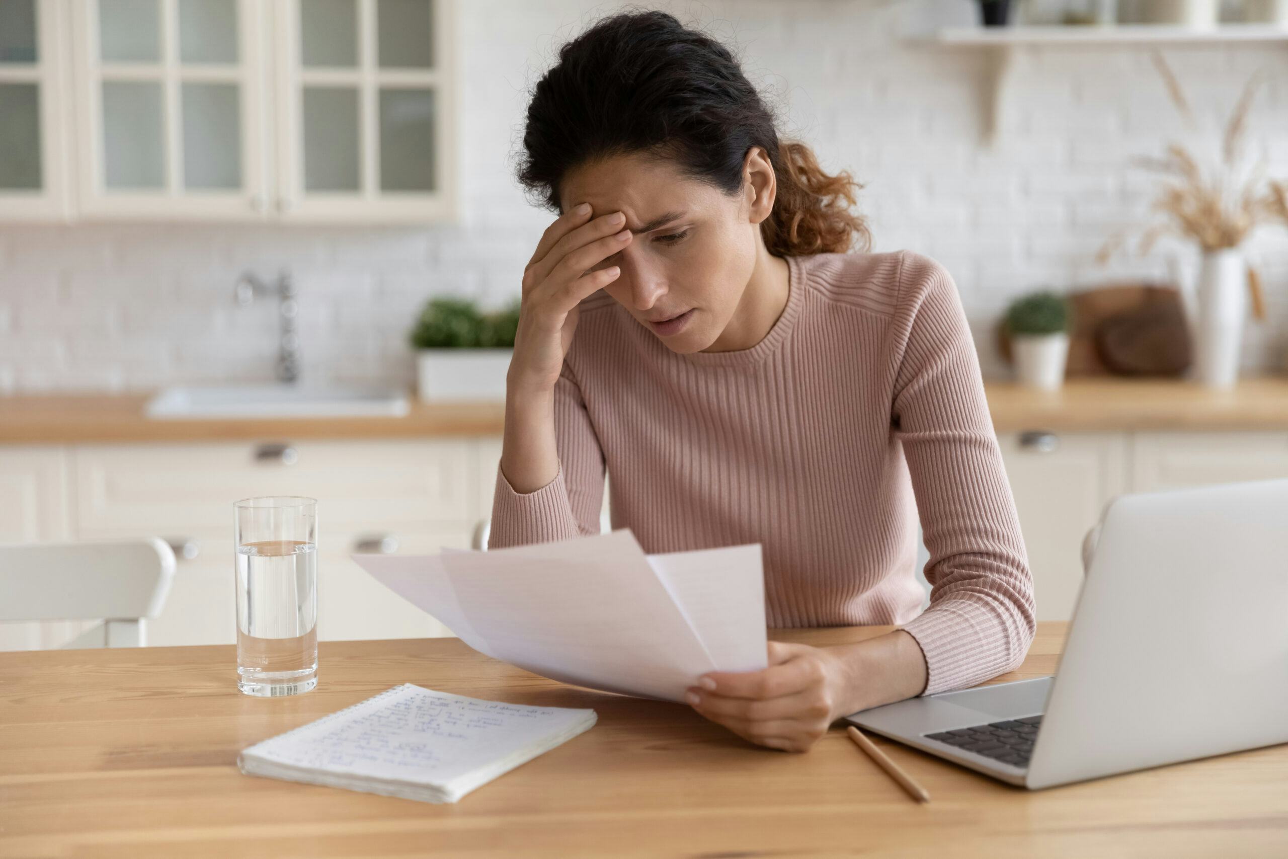 Vrouw zit achter laptop met haar hand op haar voorhoofd en leest brief